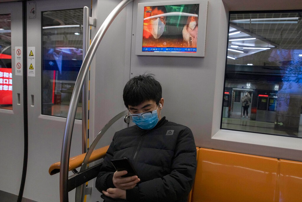 A passenger sits under a public information display encouraging the use of mask on a subway train in Beijing Monday, March 9, 2020. With almost no new COVID-19 cases being reported in Beijing, workers are slowly returning to their offices with masks on and disinfectant in hand. But officials remain cautious, torn between wanting to restart the economy and fear of a resurgence of the outbreak.