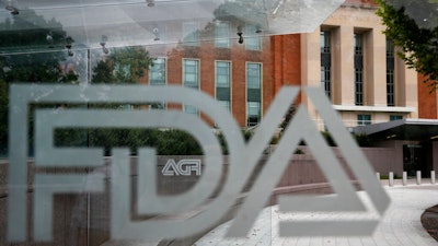 This Aug. 2, 2018, file photo shows the U.S. Food and Drug Administration building behind FDA logos at a bus stop on the agency's campus in Silver Spring, Md. Health officials reported the first U.S. drug shortage tied to the viral outbreak that is disrupting production in China, but they declined to identify the manufacturer or the product. The Food and Drug Administration said late Thursday, Feb. 27, 2020, that the drug's maker contacted health officials recently about the shortage, which it blamed on a manufacturing issue with the medicine's key ingredient.