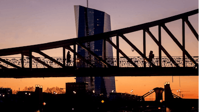 Two women walk over a bridge with the European Central Bank in background in Frankfurt, Germany, as the sun rises Monday, March 30, 2020.