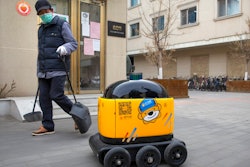 In this March 18, 2020, photo, a maintenance worker looks at a robot outside the offices of ZhenRobotics in Beijing. While other industries struggle, one robot maker says China's virus outbreak is boosting demand for his knee-high, bright yellow robots to deliver groceries and patrol malls for shoppers who fail to wear masks.