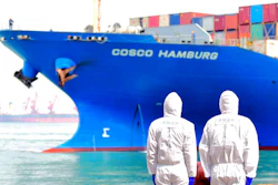 In this March 31, 2020 photo, workers in protective suits stand near a COSCO container ship docked at a port in Qingdao in eastern China's Shandong Province. China's government reported Tuesday, April 14, 2020 that exports fell further in March compared with February amid a global economic slowdown caused by the coronavirus pandemic.