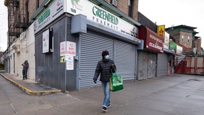 In this Friday, April 3, 2020, photo, a woman walks by local stores during the coronavirus pandemic in New York. Small business owners hoping for quick help from the government’s emergency $349 billion lending program were still waiting Tuesday, April 7, 2020, amid reports of computer problems at the Small Business Administration.