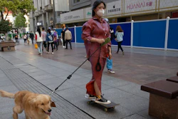 A resident gets a ride from her dog along a retail street in Wuhan in central China's Hubei province, Thursday, April 9, 2020. Released from their apartments after a 2 1/2-month quarantine, residents of the city where the coronavirus pandemic began are cautiously returning to shopping and strolling in the street but say they still go out little and keep children home while they wait for schools to reopen.