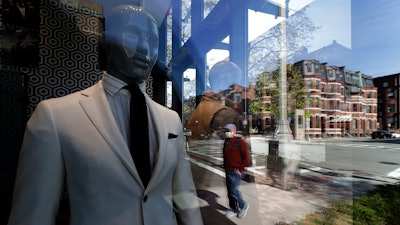 A passer-by wearing a mask out of concern for the COVID-19 coronavirus, background center, walks past mannequins in a clothing store in Boston.