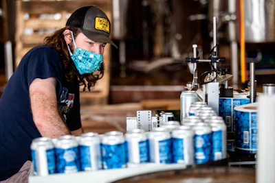 Colin Conroy operates a labeling machine as cans of 'Fauci Spring' beer are labeled at Wild Heaven Beer on Thursday, April 30 in Avondale Estates, GA.