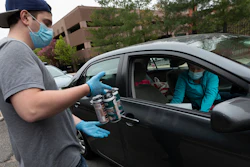 In this May 8 photo, Jack's Abby craft brewery employee Casey Mott carries an order to a customer in a line of cars waiting curbside in Framingham, MA.