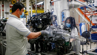 In this April 27, 2020 file photo, a plastic sheet is laid between two workers needing to face each other to perform their task, as a safety measure for coronavirus contamination, at the Fiat Chrysler Automobiles plants of Atessa, in Central Italy. Fiat Chrysler Automobiles has confirmed a request for an Italian state-backed loan to help the sector relaunch from the coronavirus shutdown, a move that set off debate in Italy over whether such money should be made available to companies with legal headquarters overseas.
