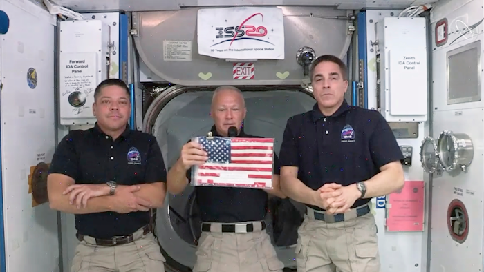 ASA astronauts Robert L. Behnken, left, and Chris Cassidy right, listen as commander Douglas Hurley speaks about retrieving the American flag left behind at the International Space Station nearly a decade ago.