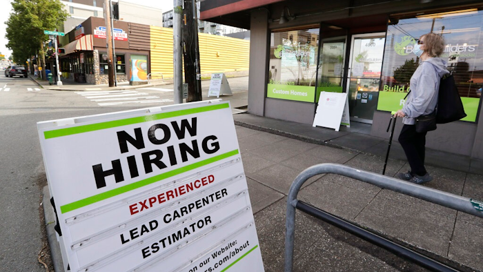 In this photo taken Thursday, June 4, 2020, a pedestrian wearing a mask walks past reader board advertising a job opening for a remodeling company, in Seattle. The U.S. unemployment rate fell to 13.3% in May, and 2.5 million jobs were added — a surprisingly positive reading in the midst of a recession that has paralyzed the economy and depressed the job market in the wake of the viral pandemic.