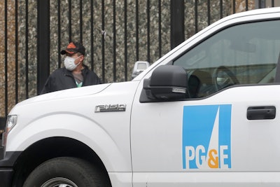 A man wearing a mask walks behind a Pacific Gas and Electric truck in San Francisco.