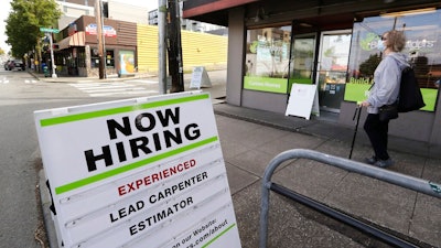 In this photo taken Thursday, June 4, 2020, a pedestrian wearing a mask walks past reader board advertising a job opening for a remodeling company, in Seattle. The U.S. unemployment rate fell to 13.3% in May, and 2.5 million jobs were added — a surprisingly positive reading in the midst of a recession that has paralyzed the economy and depressed the job market in the wake of the viral pandemic.