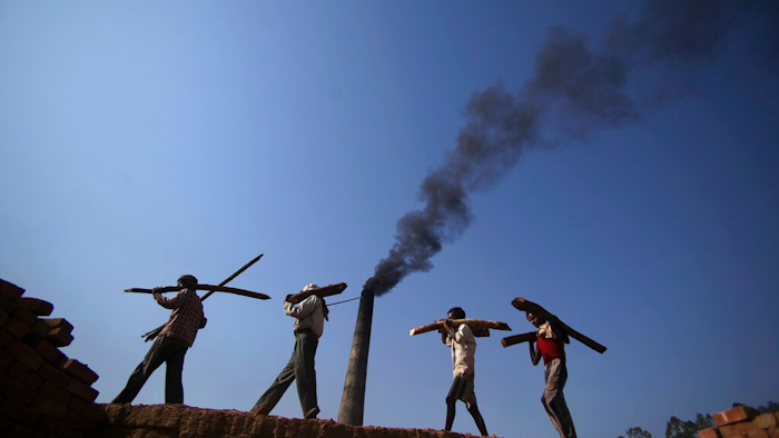 In this June 4, 2011 file photo, Indian laborers carry firewood, as smoke rises from a bricks factory on the outskirts of Jammu, India. India should commit to carbon neutrality by ending fossil fuel subsidies and investing in clean solar power as it mobilizes trillion of dollars to recover from the coronavirus pandemic, the U.N. Secretary-General António Guterres said Friday, Aug. 28, 2020.