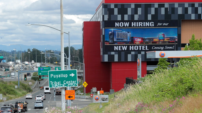 In this July 9, 2020, file photo, a large video display reads 'Now hiring for our new hotel coming soon!,' at the new Emerald Queen Casino, which is open, and owned by the Puyallup Tribe of Indians, in Tacoma, Wash. The United States added 1.8 million jobs in July, a pullback from the gains of May and June and evidence that the resurgent coronavirus has weakened hiring and the economic rebound.