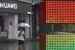 A woman wearing a mask to protect from the coronavirus walks with an umbrella as it rains outside a Huawei store.
