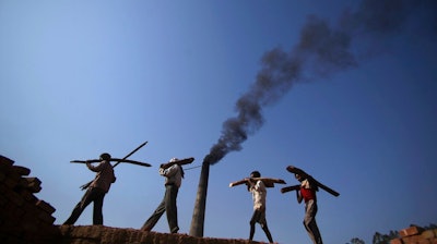 In this June 4, 2011 file photo, Indian laborers carry firewood, as smoke rises from a bricks factory on the outskirts of Jammu, India. India should commit to carbon neutrality by ending fossil fuel subsidies and investing in clean solar power as it mobilizes trillion of dollars to recover from the coronavirus pandemic, the U.N. Secretary-General António Guterres said Friday, Aug. 28, 2020.