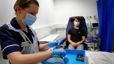 Clinical Research Nurse Aneta Gupta labels blood samples from volunteer Yash during the Imperial College vaccine trial, at a clinic in London, Wednesday, Aug. 5, 2020. Scientists at Imperial College London are immunizing hundreds of people with an experimental coronavirus vaccine in an early trial after seeing no worrying safety problems in a small number vaccinated so far.