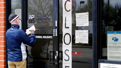 In this April 30, 2020 file photo, a man writes information in front of Illinois Department of Employment Security in Chicago. It's the paradox of a pandemic that has crushed the U.S. economy: There are 12.9 million job losses and a dangerous rash of closed business, yet the personal finances of many Americans have remained strong, and in some ways have even improved. A new poll by The Associated Press-NORC Center for Public Affairs Research shows that 45% of Americans say they’re setting aside more money than usual. Twenty-six percent are paying down debt faster than they were before the coronavirus pandemic. In total, about half of Americans say they’ve either saved more or paid down debt.