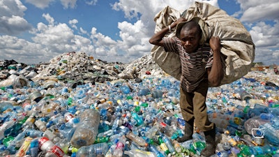A man walks on a mountain of plastic bottles.