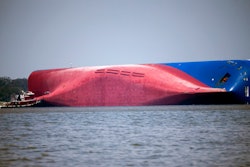 In this Sept. 9, 2019, file photo, a Moran tugboat nears the stern of the capsizing vessel Golden Ray near St. Simons Sound off the coast of Georgia. The salvage team is seeking a federal permit to surround the shipwreck with a giant mesh barrier to contain any debris when they cut the ship apart. Salvage workers coming to the Georgia coast to cut apart and remove the cargo ship that overturned will be isolated at a nearby resort to protect them from the coronavirus, officials said Tuesday, Sept. 8, 2020.