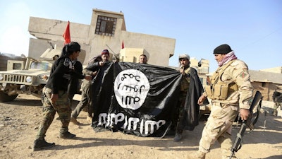 Iraqi Army soldiers celebrate as they hold a flag of the Islamic State group captured during a military operation to regain control of a village outside Mosul, Iraq, Nov. 29, 2016.