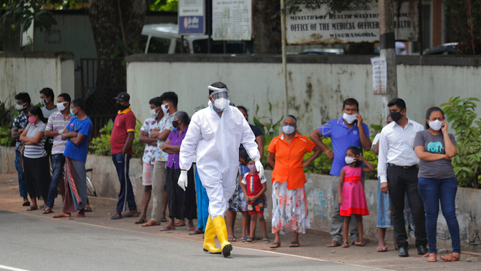 Sri Lankans wait to give swab samples to test for COVID-19 outside a hospital as a health official walks past in Minuwangoda, Sri Lanka.