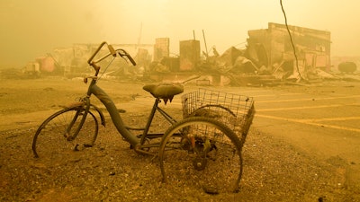 A trike stands near the burnt remains of a building destroyed by a wildfire.