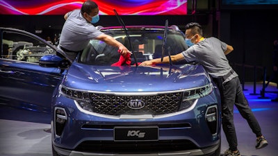 Staff members wearing face masks to protect against the coronavirus clean a Kia KX5 compact SUV.