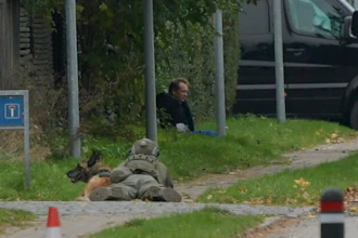 A police office watches Peter Madsen as he sits on the side of a road after being apprehended following a failed escape attempt.