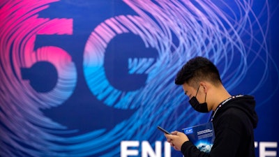 A man looks at his smartphone as he walks past a sign advertising 5G services at the PT Expo in Beijing.