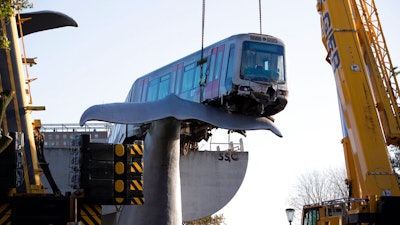 A salvaging crew prepares to attach chains to lift to a metro train carriage off the whale's tail.