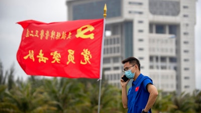 A worker talks on a cellphone near a flag with the logo of the Communist Party of China at the Wenchang Space Launch Site in Wenchang in southern China's Hainan province, Monday, Nov. 23, 2020. Chinese technicians were making final preparations Monday for a mission to bring back material from the moon's surface for the first time in nearly half a century — an undertaking that could boost human understanding of the moon and of the solar system more generally.