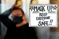 In this Tuesday, Nov. 17, 2020 file photo, manager Yllka Murati waits for a delivery driver to pick up takeout orders behind a partition displaying a sign to remind customers to wear a mask, at the Penrose Diner, in south Philadelphia.