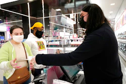 Cashier Druhan Parker, right, works behind a plexiglass shield Thursday, Nov. 19, 2020, as he checks out shoppers Cassie Howard, left, and Paris Black at an in Chicago. The accelerating surge of coronavirus cases across the U.S. is causing an existential crisis for America’s retailers and spooking their customers just as the critically important holiday shopping season nears.