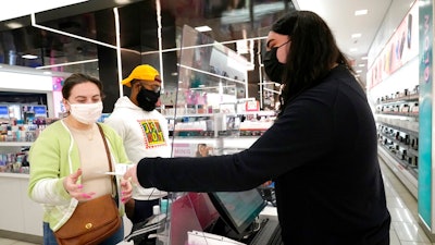 Cashier Druhan Parker, right, works behind a plexiglass shield Thursday, Nov. 19, 2020, as he checks out shoppers Cassie Howard, left, and Paris Black at an in Chicago. The accelerating surge of coronavirus cases across the U.S. is causing an existential crisis for America’s retailers and spooking their customers just as the critically important holiday shopping season nears.