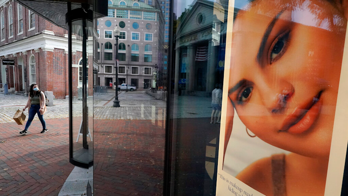 A woman carries a shopping bag while walking past a cosmetics store.