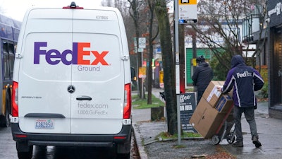 A driver with FedEx carries a package away from a van, Tuesday, Dec. 8, 2020, in Seattle.