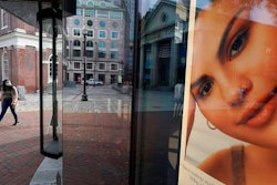 A woman carries a shopping bag while walking past a cosmetics store.