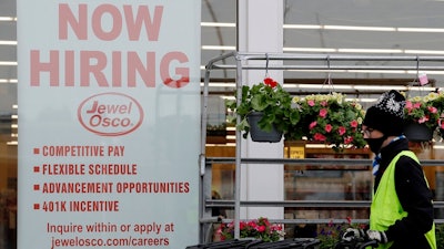 A man pushes carts as a hiring sign shows at a Jewel Osco grocery store in Deerfield, Ill., Thursday, April 23, 2020. Friday, Dec. 4, monthly U.S. jobs report will help answer a key question hanging over the economy: Just how much damage is being caused by the resurgent coronavirus, the resulting restrictions on businesses and the reluctance of consumers to shop, travel and dine out?
