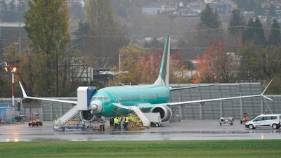 In this Nov. 18, 2020 photo, workers stand near a Boeing 737 Max airplane parked at Renton Municipal Airport next to the Boeing assembly facility in Renton, WA, where 737 Max airplanes are made.