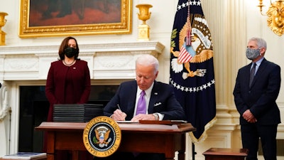 President Joe Biden signs executive orders after speaking about the coronavirus, accompanied by Vice President Kamala Harris, left, and Dr. Anthony Fauci, director of the National Institute of Allergy and Infectious Diseases, right, in the State Dinning Room of the White House, Thursday, Jan. 21, 2021, in Washington.