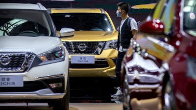 In this file photo, a visitor wearing a face mask to protect against the coronavirus walks among vehicles from Nissan at the Beijing International Automotive Exhibition, also known as Auto China, in Beijing.