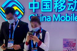 In this Oct. 14, 2020 file photo, staff members wearing face masks to protect against the spread of the coronavirus use their smartphones at a display from Chinese telecommunications firm China Mobile at the PT Expo in Beijing. The New York Stock Exchange is going ahead with plans to delist shares of three Chinese state-owned phone carriers under an executive order from President Donald Trump. The exchange said trading in the three companies, China Telecom Corp. Ltd., China Mobile Ltd. and China Unicom Hong Kong Ltd., will be suspended after the markets close on Jan. 11, 2021.