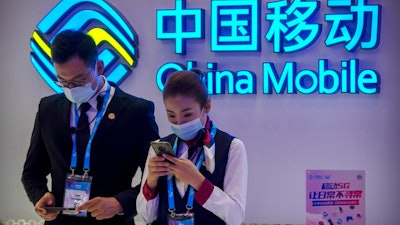In this Oct. 14, 2020 file photo, staff members wearing face masks to protect against the spread of the coronavirus use their smartphones at a display from Chinese telecommunications firm China Mobile at the PT Expo in Beijing. The New York Stock Exchange is going ahead with plans to delist shares of three Chinese state-owned phone carriers under an executive order from President Donald Trump. The exchange said trading in the three companies, China Telecom Corp. Ltd., China Mobile Ltd. and China Unicom Hong Kong Ltd., will be suspended after the markets close on Jan. 11, 2021.