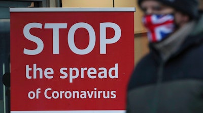 A man wearing a British union flag face mask walks past a coronavirus advice sign outside a bank in Glasgow the morning after stricter lockdown measures came into force for Scotland, Tuesday Jan. 5, 2021. Further measures were put in place Tuesday as part of lockdown restrictions in a bid to halt the spread of the coronavirus.
