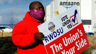 Michael Foster of the Retail, Wholesale and Department Store Union holds a sign outside an Amazon facility where labor is trying to organize workers on Tuesday, Feb. 9, 2021. For Amazon, a successful effort could motivate other workers to organize. But a contract could take years, and Amazon has a history of crushing labor organizing.