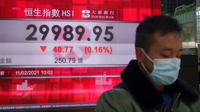 A man wearing a face mask walks past a bank's electronic board showing the Hong Kong share index in Hong Kong, Thursday, Feb. 11, 2021. Despite a short drop in early trading in Hong Kong, most major Asian stock indexes were higher on Thursday after President Joe Biden held his first conversation with Chinese leader Xi Jinping since taking office.