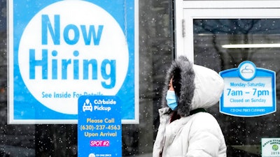 In this Feb. 6, 2021 file photo, a woman walks past a 'Now Hiring' sign displayed at a CD One Price Cleaners in Schaumburg, Ill. In a stark sign of the economic inequality that has marked the pandemic recession and recovery, Americans as a whole are now earning the same amount of wages and salaries that they did before the pandemic struck, even with nearly 9 million fewer people at work.
