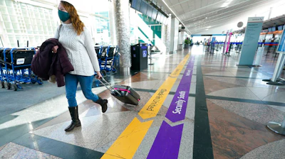 In this Feb. 18 photo, a lone traveler wears a face covering while hurrying through a near-empty check-in counter area in the main terminal of Denver International Airport.