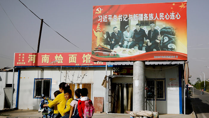 In this Sept. 20, 2018, file photo, an Uyghur woman uses an electric-powered scooter to fetch school children as they ride past a picture showing China's President Xi Jinping joining hands with a group of Uighur elders.