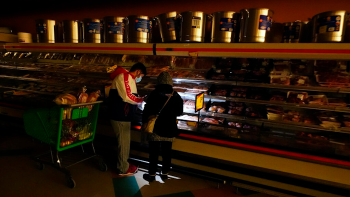 In this Tuesday, Feb. 16, 2021 file photo, customers use the light from a cell phone to look in the meat section of a grocery store that was without power, in Dallas. Brazos Electric Power Cooperative Inc., the oldest and biggest generation and transmission power cooperative in Texas has filed for Chapter 11 bankruptcy protection following last month’s winter storm that left millions without power.